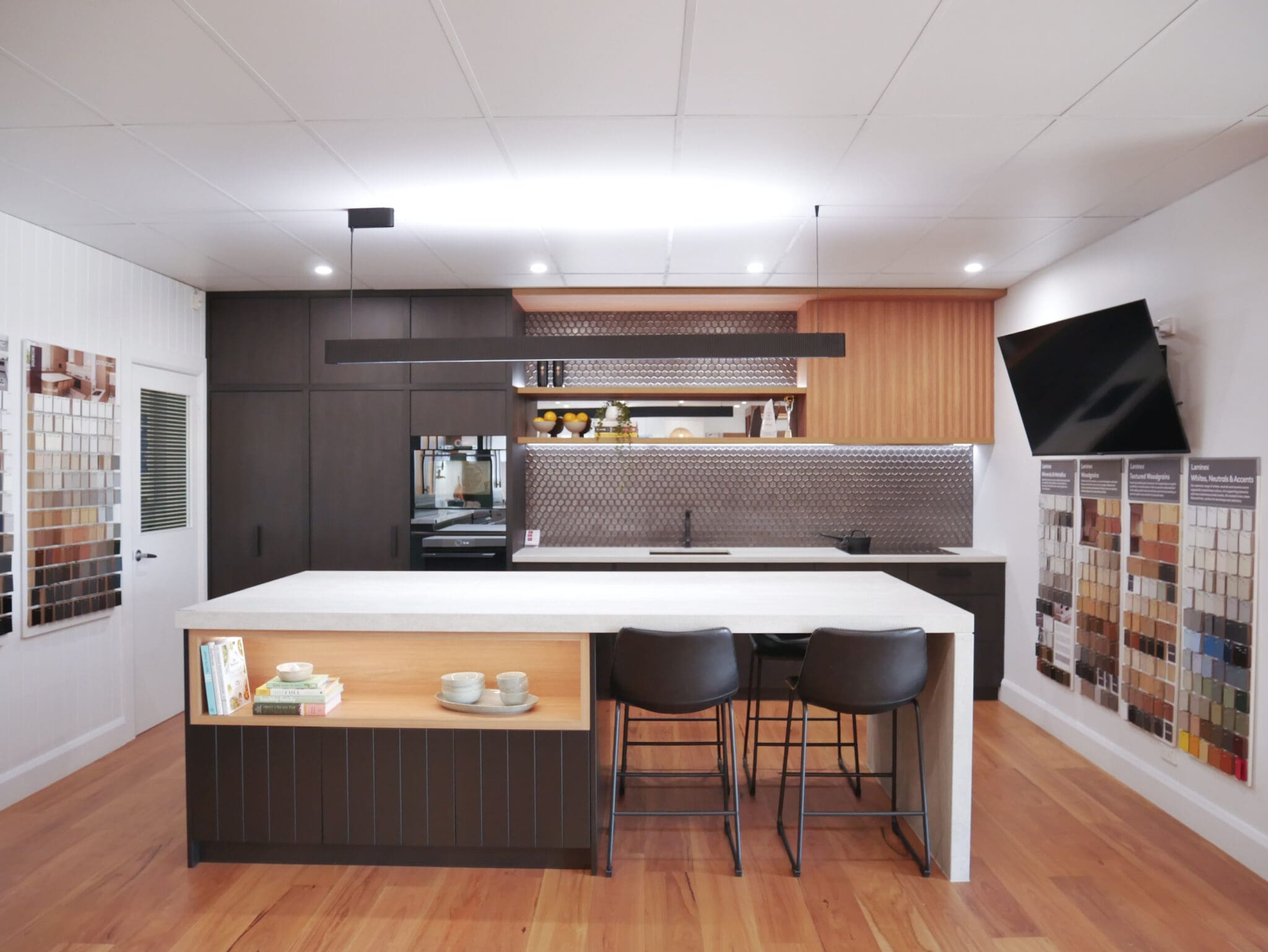 Harrington Kitchens Narellan Kitchen Showroom featuring stone waterfall island with open timber shelves. 