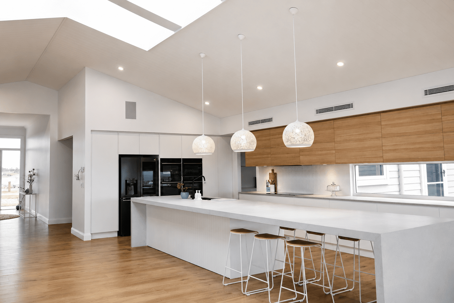 Bright modern kitchen with a large waterfall stone kitchen island, timber overhead cabinetry, pendant lighting and skylight ceiling in a contemporary open-plan home.