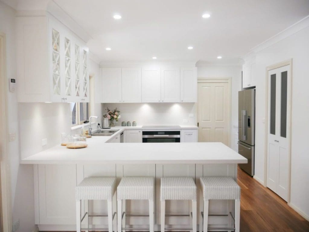 Muted white and grey Hamptons kitchen with elegant bar seating and bright kitchen ceiling lights for a warm, inviting atmosphere.