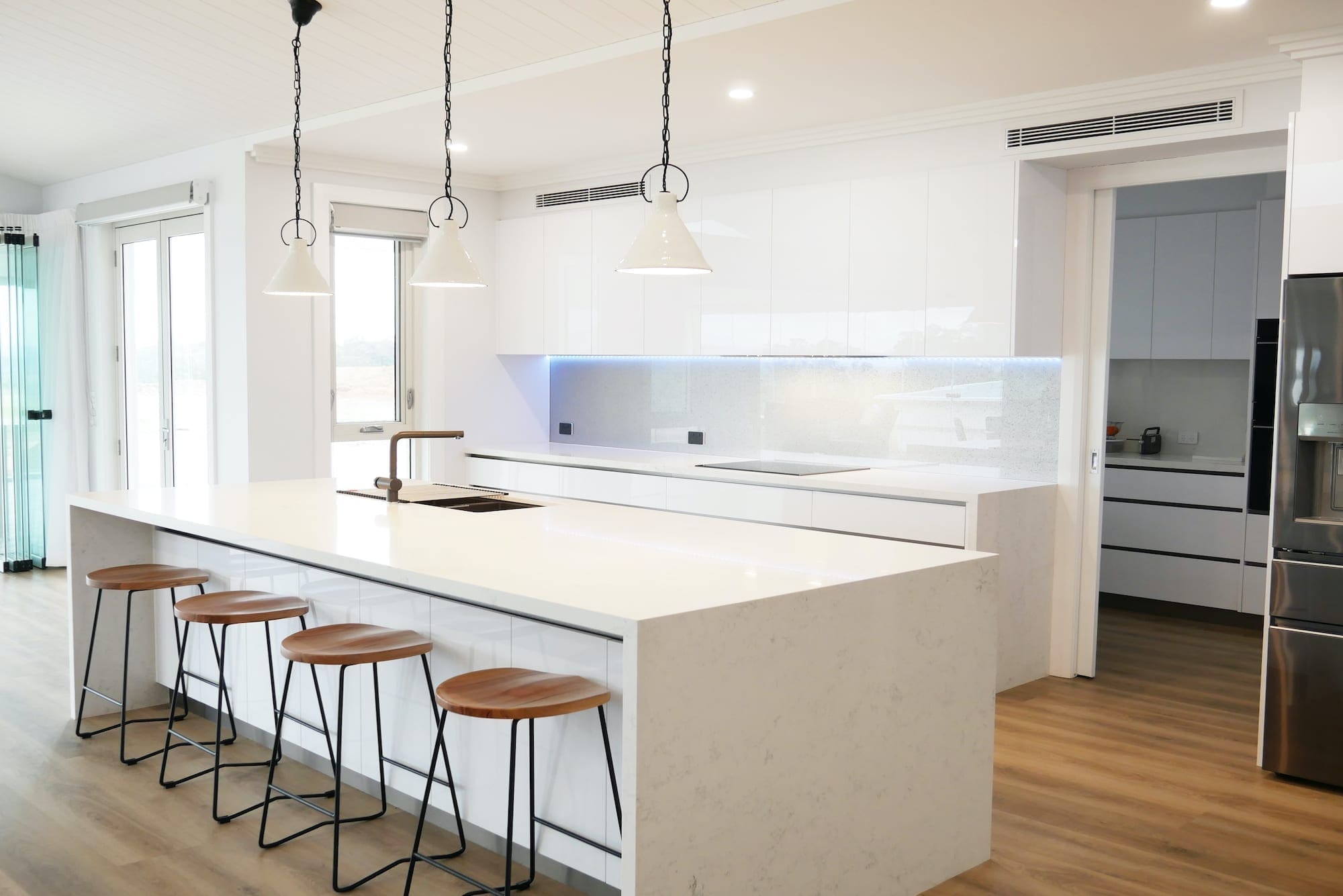Modern white perfection kitchen Razorback with white stone waterfall benchtops and three handing pendant lights