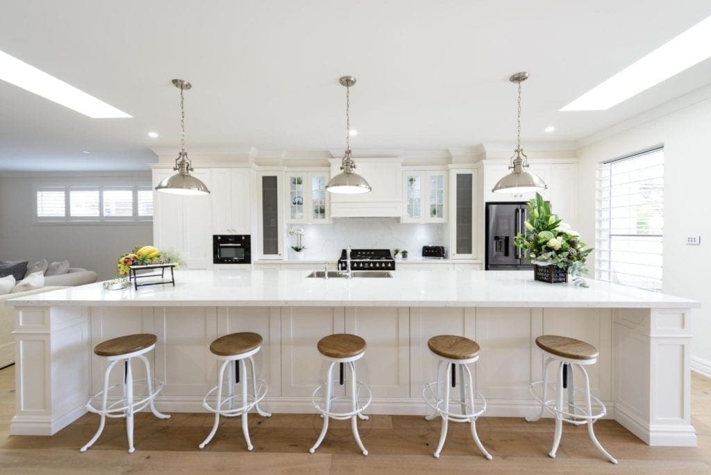 Bright Hamptons-style kitchen with an oversized island bench, industrial stools, and pendant lighting.