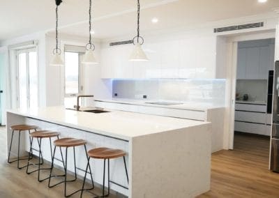 Modern white perfection kitchen Razorback with white stone waterfall benchtops and three handing pendant lights