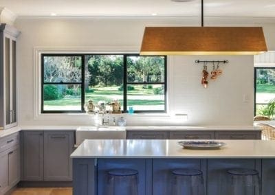 timeless and subtle hamptons kitchen with hanging light pendant and green gras view window