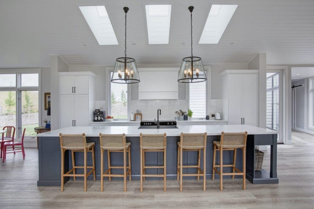 Spacious Hamptons-style kitchen with a large navy island bench, timber bar stools, and pendant lighting under skylights.