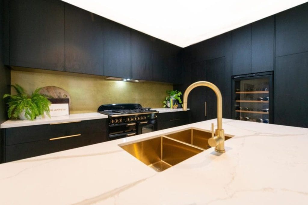 Modern black kitchen with a marble island bench, gold tapware, and integrated sink.