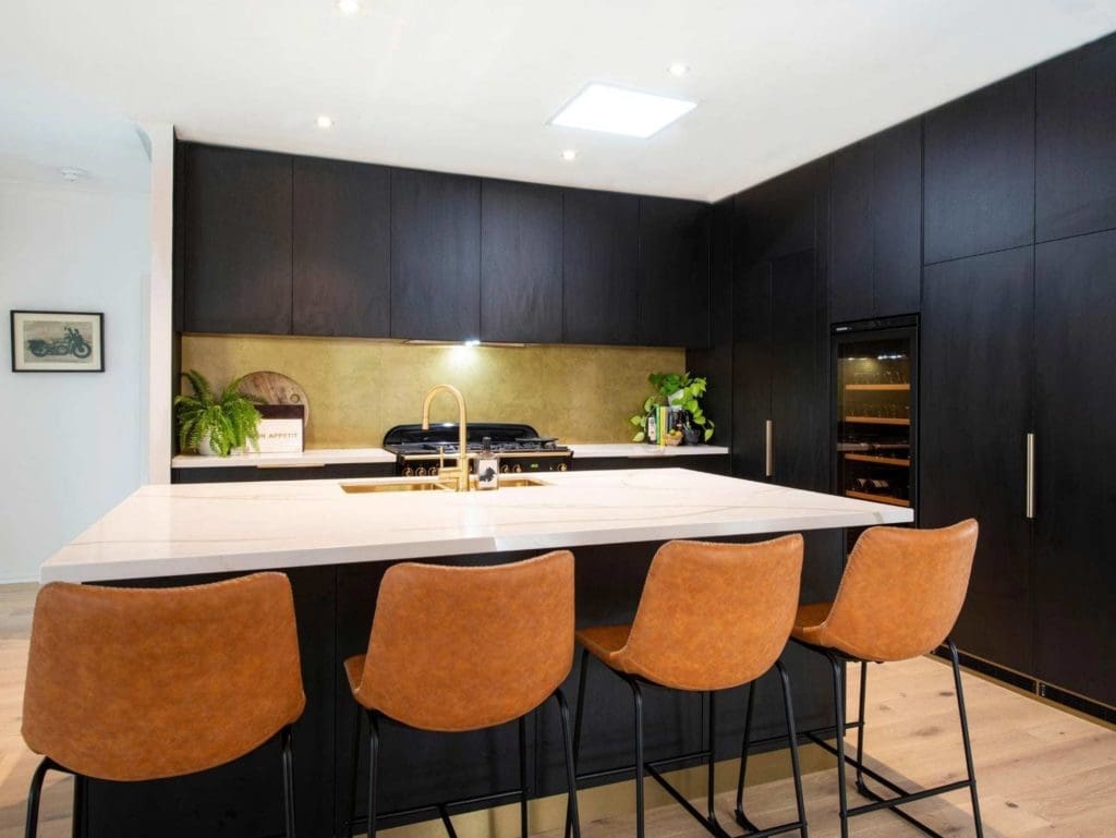 Modern kitchen renovation in Sydney featuring matte black cabinetry, gold accents, and a large island with leather bar stools.