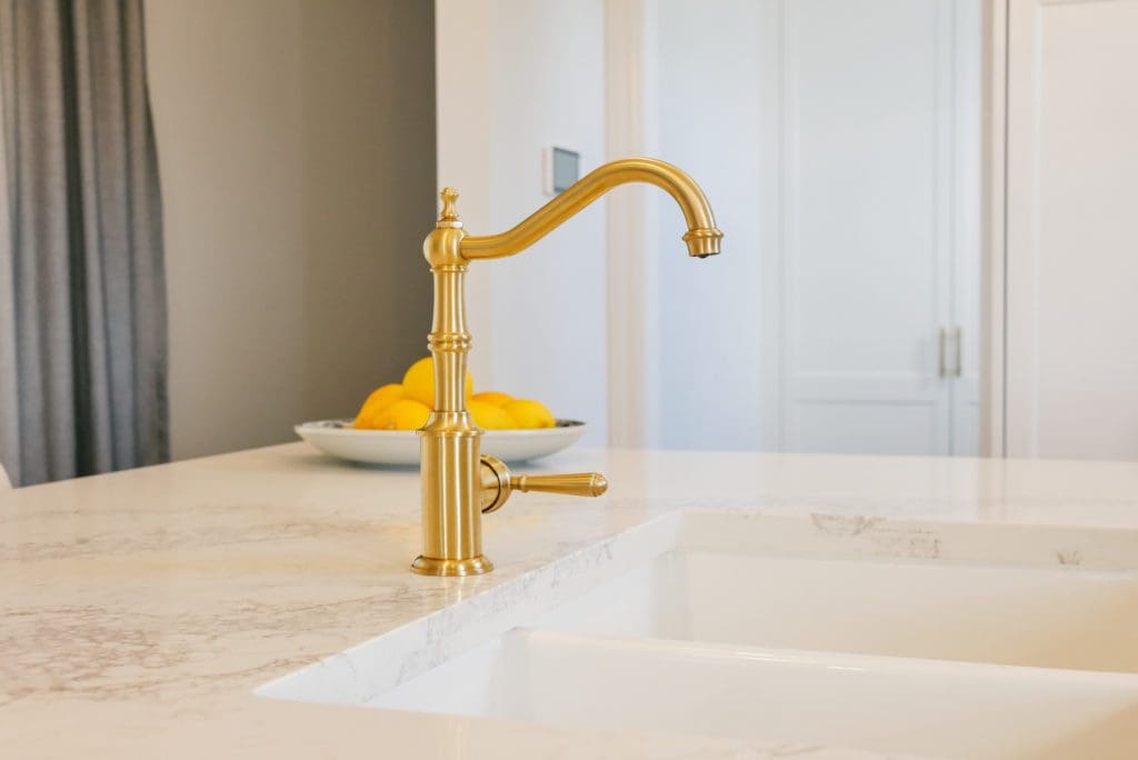 Close-up of a gold mixer tap on a marble kitchen island bench with a bowl of lemons in the background.