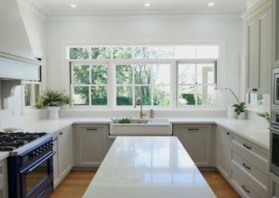 modern farmhouse kitchen featuring provincial cabinetry, farmhouse sink, brushed brass tapware, and a large window overlooking a lush green garden.
