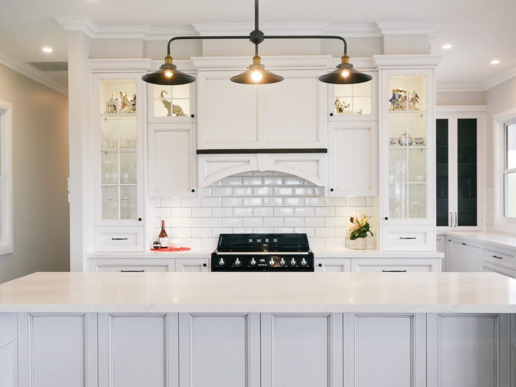 Modern country-style kitchen with white cabinetry, subway tile splashback, and black pendant lighting above a large island bench.