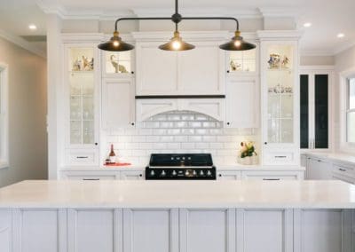 Modern country-style kitchen with white cabinetry, subway tile splashback, and black pendant lighting above a large island bench.