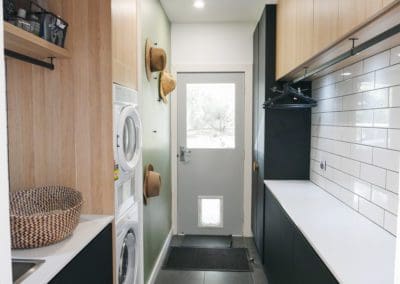 Spacious walk-in pantry behind the pantry doors, created by expanding the kitchen area into the laundry. The renovation included removing walls, framing new structures, and installing new cabinetry. The cold concrete floors were replaced with warm natural timber, accommodating the sink on the island.