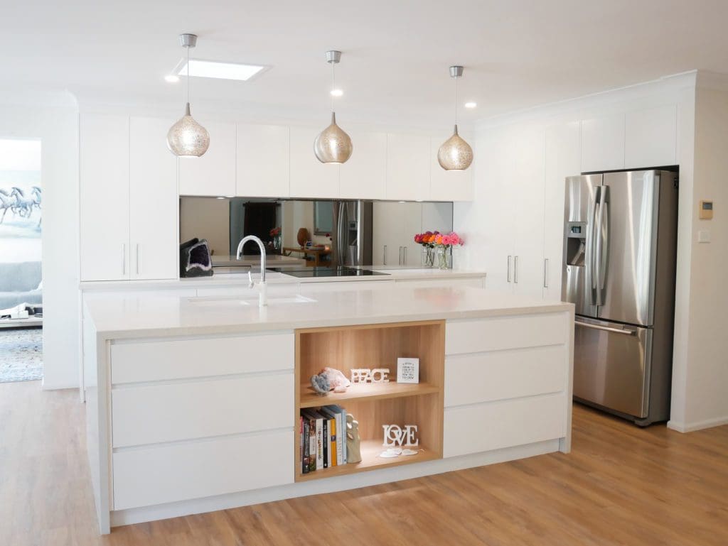 Modern white kitchen with mirrored splashback, pendant lights, and a central island featuring open shelving.