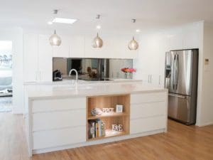 Modern white kitchen with mirrored splashback, pendant lights, and a central island featuring open shelving.