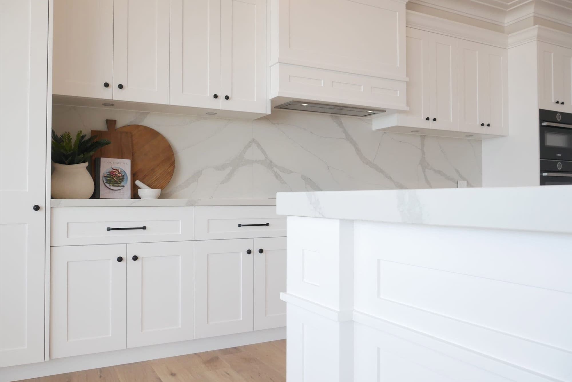 Modern white kitchen with marble-look benchtops, shaker cabinetry, black SMEG oven, and matte black fixtures.