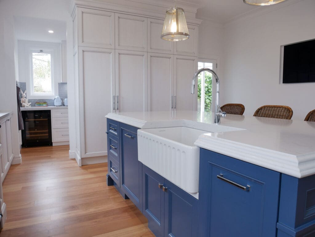 Quality kitchen cabinets surrounding a striking blue island bench with a classic farmhouse sink, blending modern craftsmanship with timeless charm
