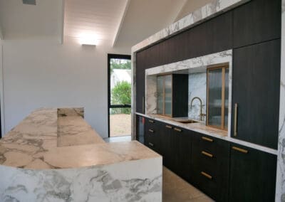 Bar side of the kitchen featuring a full Calacatta Vagili marble splashback, Titan brass undermount sink, and matching brass Titan tap. Aluminium doors with brass finish and fluted glass inserts frame the bar, with glass shelves inside the push-to-open doors.