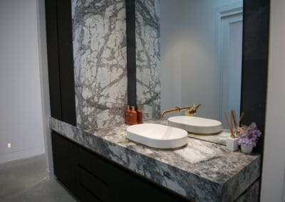 Guest vanity featuring Navurban Ravenswood cabinetry, Cote D’Azur marble benchtop with 150mm mitred edges, and elegant wall cladding. A Caroma vanity bowl sits atop the stone with a floating Astra Walker wall mixer tap, complemented by a glass mirror splashback.