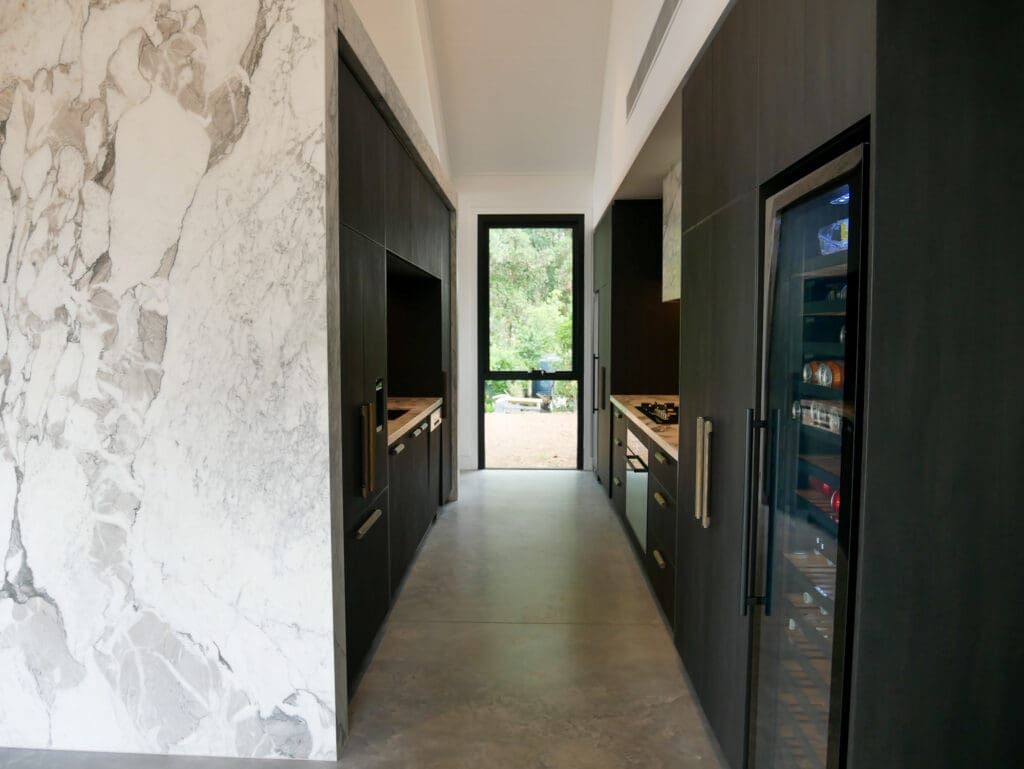 Bar side of the kitchen featuring full Calacatta Vagili marble splashback, Titan brass undermount sink, and matching brass Titan tap. Aluminium doors with brass finish and fluted glass inserts frame the bar, with glass shelves inside the push-to-open doors.