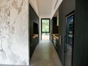 Bar side of the kitchen featuring full Calacatta Vagili marble splashback, Titan brass undermount sink, and matching brass Titan tap. Aluminium doors with brass finish and fluted glass inserts frame the bar, with glass shelves inside the push-to-open doors.