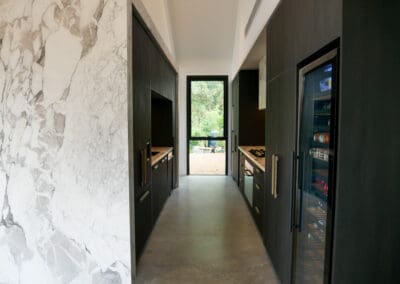 Bar side of the kitchen featuring full Calacatta Vagili marble splashback, Titan brass undermount sink, and matching brass Titan tap. Aluminium doors with brass finish and fluted glass inserts frame the bar, with glass shelves inside the push-to-open doors.