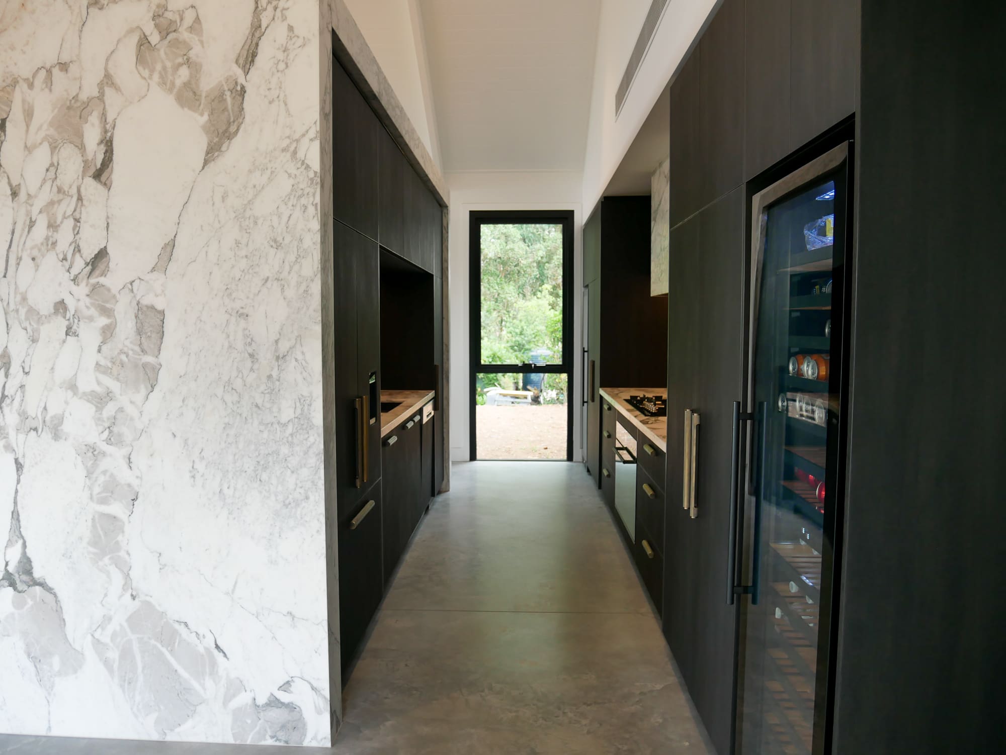 Bar side of the kitchen featuring full Calacatta Vagili marble splashback, Titan brass undermount sink, and matching brass Titan tap. Aluminium doors with brass finish and fluted glass inserts frame the bar, with glass shelves inside the push-to-open doors.