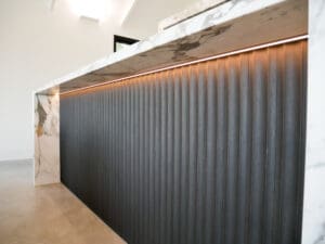 Modern kitchen benchtop with Calacatta marble waterfall edges and fluted dark timber paneling.
