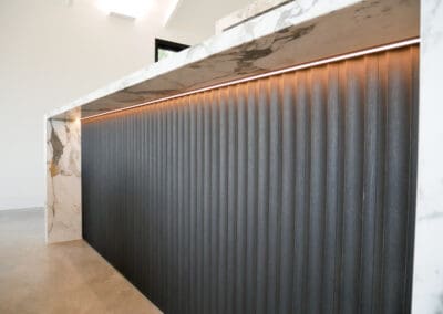 Modern kitchen benchtop with Calacatta marble waterfall edges and fluted dark timber paneling.