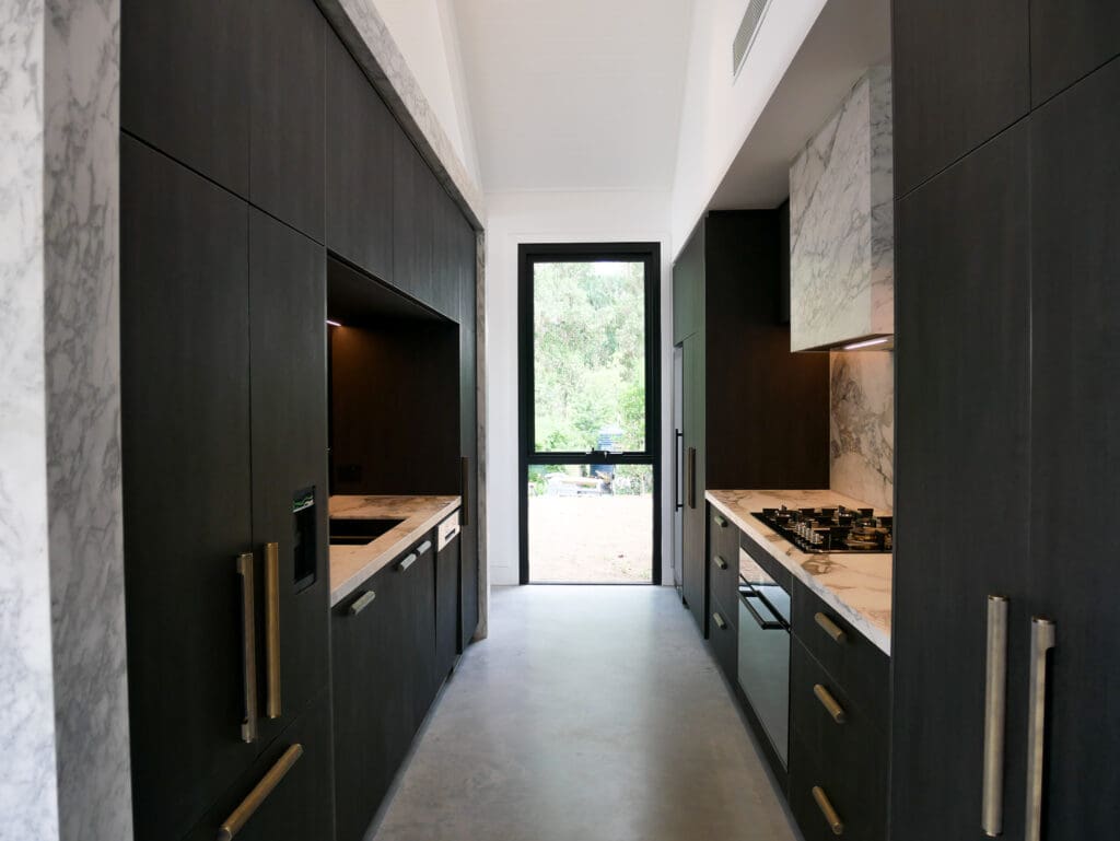 Bar side of the kitchen featuring full Calacatta Vagili marble splashback, Titan brass undermount sink, and matching brass Titan tap. Aluminium doors with brass finish and fluted glass inserts frame the bar, with glass shelves inside the push-to-open doors.