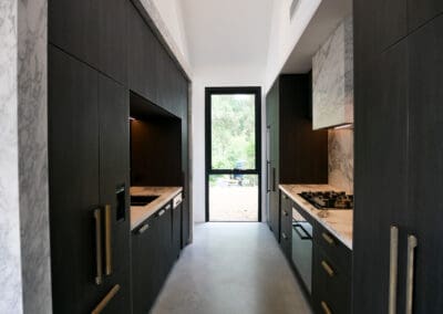 Bar side of the kitchen featuring full Calacatta Vagili marble splashback, Titan brass undermount sink, and matching brass Titan tap. Aluminium doors with brass finish and fluted glass inserts frame the bar, with glass shelves inside the push-to-open doors.