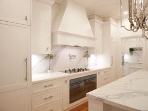 Kitchen featuring Dulux Lexicon matte finish, Colorado profile cabinetry, Quantum Quartz Alpine White benchtops, and Classico Palazzo splashbacks. Includes a hidden Falmec rangehood, Smeg integrated fridge/freezer, and polished nickel pot filler above the cooktop.