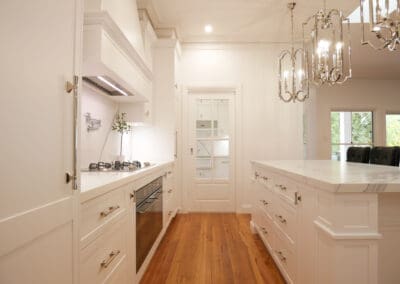 Kitchen with Dulux Lexicon matte finish, Colorado profile cabinetry, Quantum Quartz Alpine White benchtops, and Classico Palazzo splashbacks. Hidden Falmec rangehood, Smeg integrated fridge/freezer, and polished nickel pot filler above the cooktop
