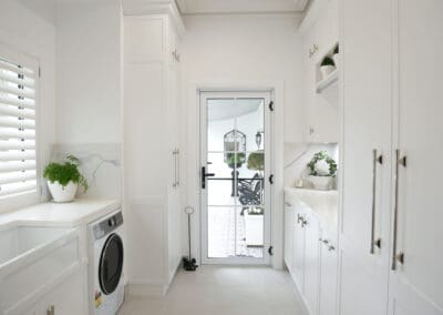Laundry featuring a 1901 single butler's sink with a washing machine and dryer on either side, complemented by polished nickel Momo Pembrey handles and knobs for a touch of elegance.