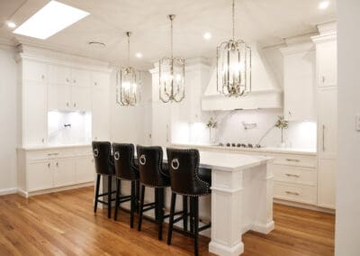 Kitchen featuring three polished nickel pendants over a stunning island with leather bar chairs. Dulux Lexicon quarter strength matte finish and modern Colorado profile cabinetry with decorative capping. Quantum Quartz Alpine White benchtops and Classico Palazzo splashbacks with grey veining, complementing the elegant design.
