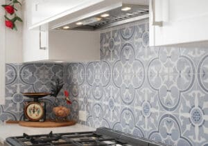 X-Frame glass cabinet doors decorate the top of the wall cabinetry, adding a traditional touch to the modern kitchen, further highlighted by the striking blue and black handcrafted tiles on the splashback.