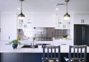 Brushed brass and matte black pendants over the island complement the Statue Bronze Brodware Winslow tap, black granite sink, and handmade brass and black wooden handles. The Bosch rangehood with glass inset doors and underbench lighting highlights a unique Pewter-finished splashback with handmade Spanish tiles.