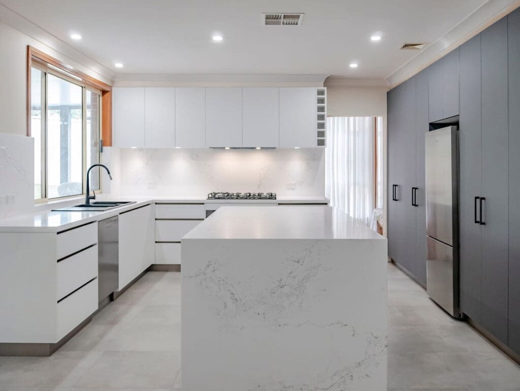 Modern kitchen featuring a sleek marble-look kitchen island with matte cabinetry and integrated appliances.
