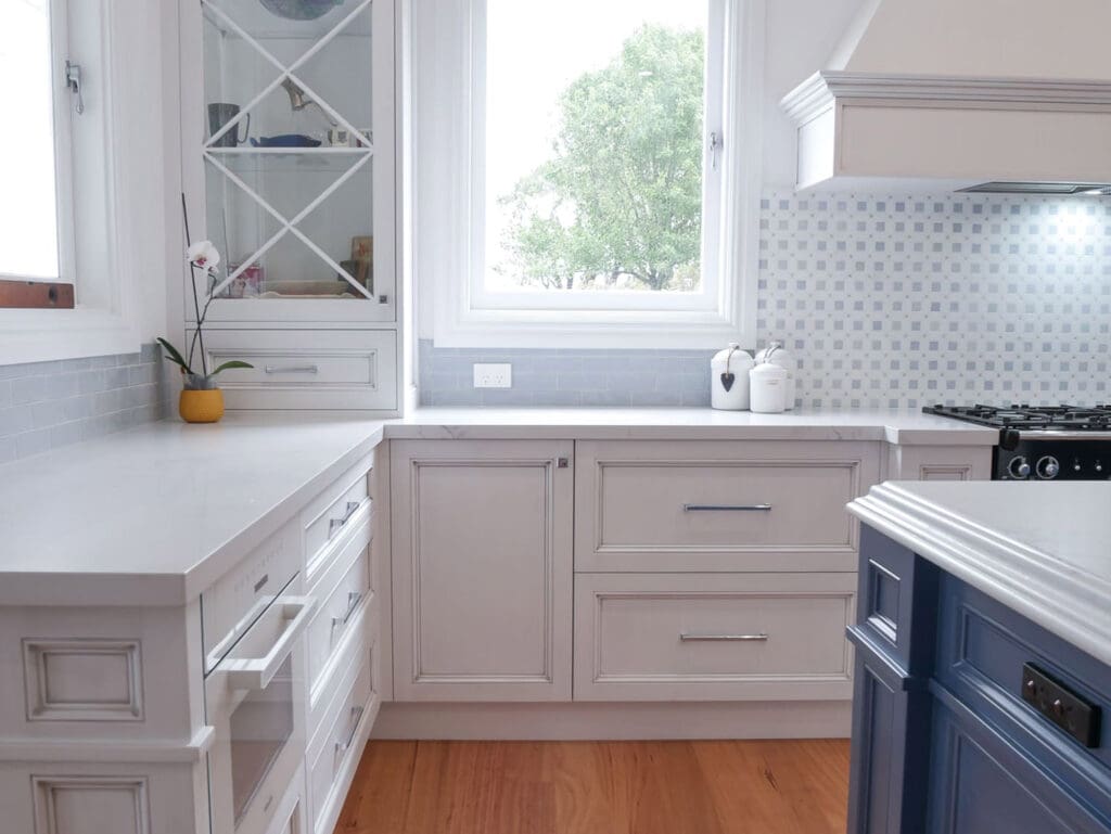 Natural light fills the kitchen, accentuating the beautiful medium antiqued hand-painted cabinetry, featuring Dulux Lexicon quarter strength over rich Dulux Domino.