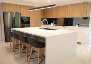 Two-tone ultra-modern kitchen with matte poly Lexicon quarter strength lower cabinetry matching the floor tiles, and Polytec Natural Oak upper cabinetry, adding warmth and dimension, complementing the stack stone feature walls.
