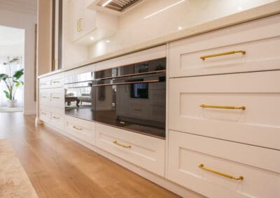 Kitchen with a warm bronze theme, featuring Rounded Bugle Kethy handles in matte brass finish and double 900 ovens with hamptons profile drawers.
