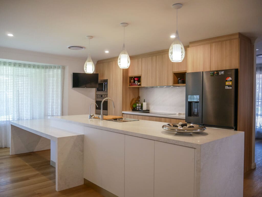 A two-toned kitchen design featuring flat matte polyurethane in Lexicon quarter for the lower island bench cabinets, Polytech Plantation Ash on the wall cabinetry, and YDL’s elegant Summer Breeze stone, creating a stylish and inviting natural texture.