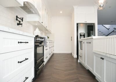 Side view of a white provincial kitchen with shaker cabinets, cross-glass upper doors, and marble-look benchtops.