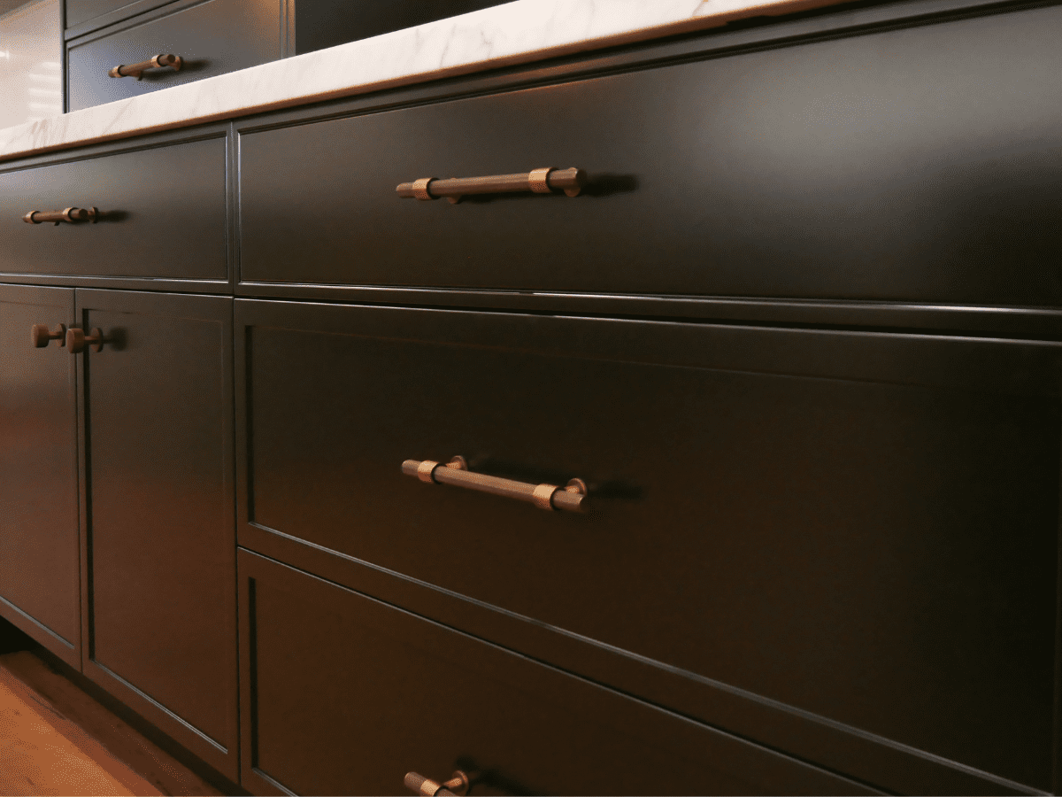 Kitchen Handles Modern white kitchen with gold handles on drawers and cabinets, featuring a black freestanding oven and glossy light grey subway tile backsplash.