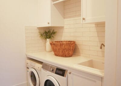 Compact white laundry with shaker cabinetry, front-loading appliances, patterned floor tiles, and a built-in sink.