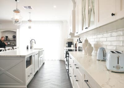 Side view of a white provincial kitchen with shaker cabinets, cross-glass upper doors, and marble-look benchtops.
