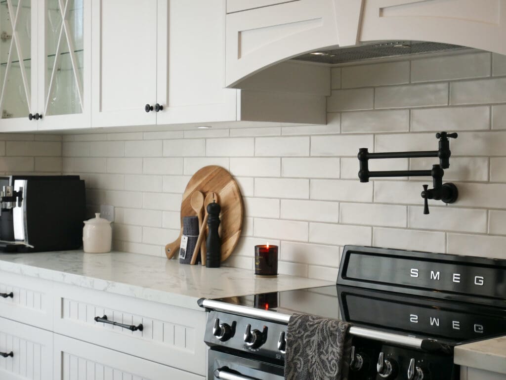 Luxury white provincial kitchen with glass-front cabinets, marble-look benchtops, black SMEG oven, and matte black pot filler.