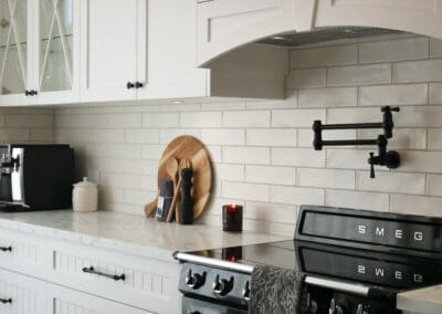 Luxury white provincial kitchen with glass-front cabinets, marble-look benchtops, black SMEG oven, and matte black pot filler.
