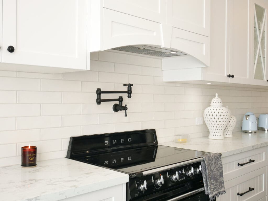 Custom-built white rangehood above a black SMEG oven with matte black pot filler and subway tile splashback.