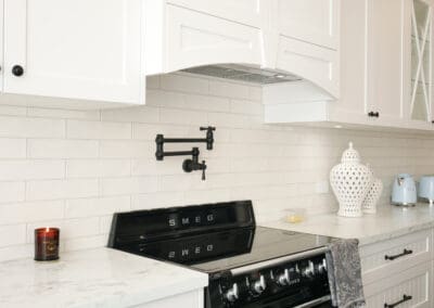 Custom-built white rangehood above a black SMEG oven with matte black pot filler and subway tile splashback.