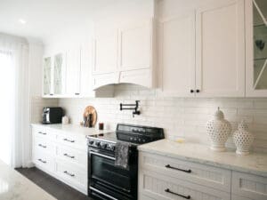 Custom-built white rangehood above a black SMEG oven with matte black pot filler and subway tile splashback.
