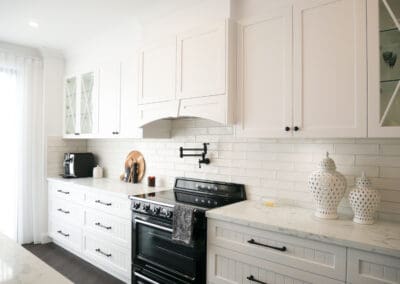 Custom-built white rangehood above a black SMEG oven with matte black pot filler and subway tile splashback.